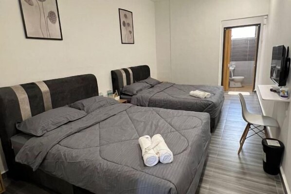 A hotel room with two beds, a desk, a chair, and a TV.