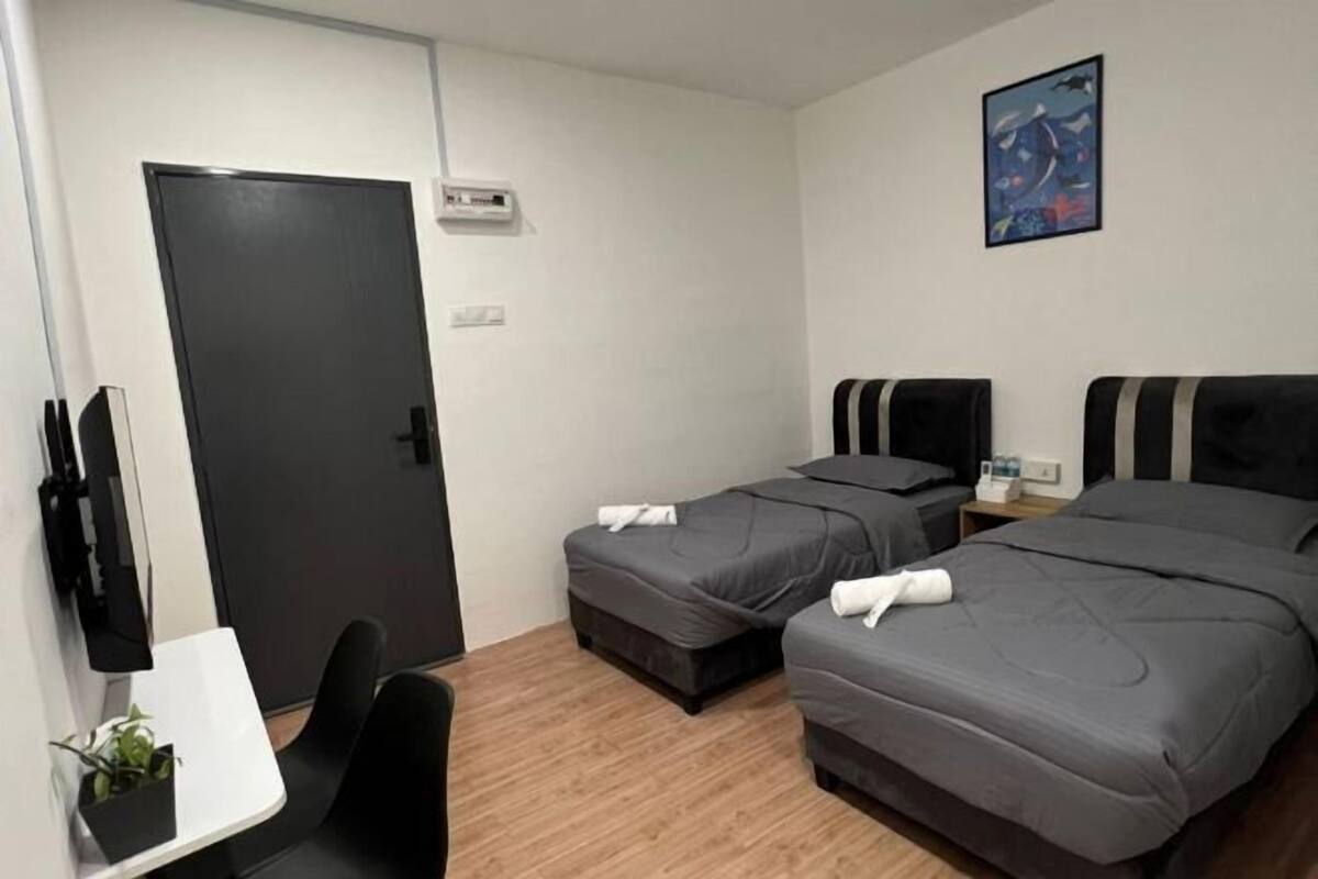 Hotellihuone, jossa on kaksi sänkyä, työpöytä, tuoli, pieni pöytä, jossa on kasvi, ovi ja seinälle asennettu ilmastointilaite.