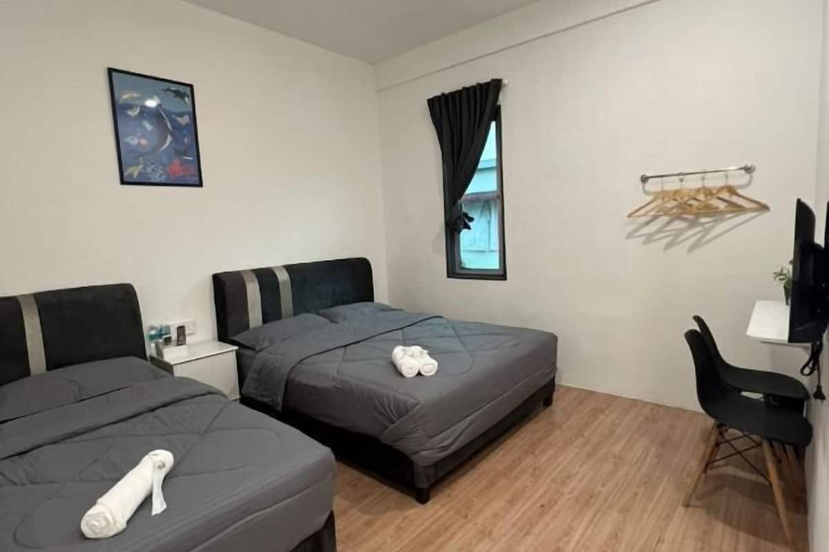 Hotellihuone, jossa on kaksi sänkyä, työpöytä, tuoli, ikkuna verhoilla, seinälle kiinnitetty naulakko ja taulu.
