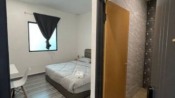 A bedroom with a bed, a desk, a chair, and a window with a curtain.
