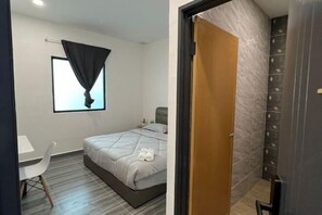 A bedroom with a bed, a desk, a chair, and a window with a curtain.