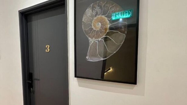 A door with the number 3 and a wall-mounted artwork of a shell with a neon exit sign. - Kiwi Inn (Pengkalan Aor)