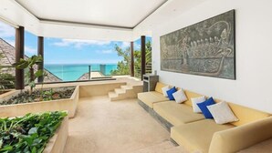 A modern living room with a large window overlooking a pool and ocean, a beige sofa with cushions, and a large abstract painting on the wall. - Jasmine Waterslide 5BR Pool Villa (Koh Samui)
