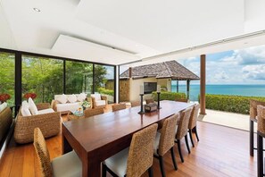 Een moderne eethoek met een houten tafel en rieten stoelen, met uitzicht op een schilderachtig zeegezicht.