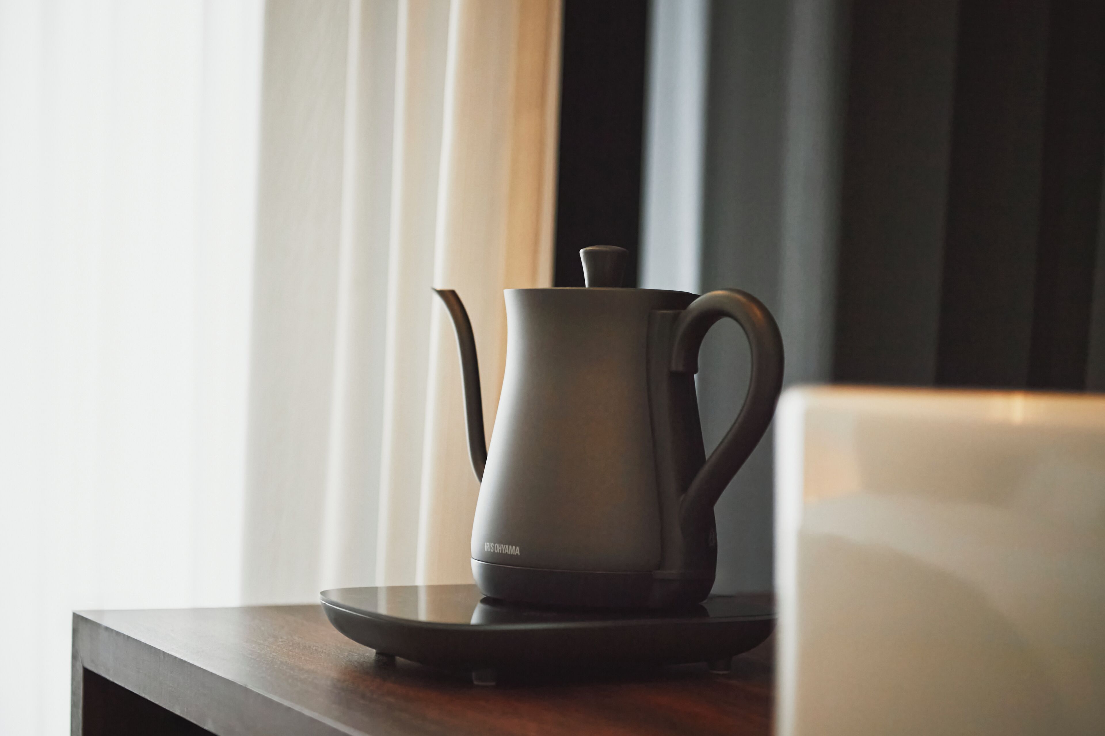 A modern kitchen with a kettle on a tray, a coffee maker, and a window with curtains.