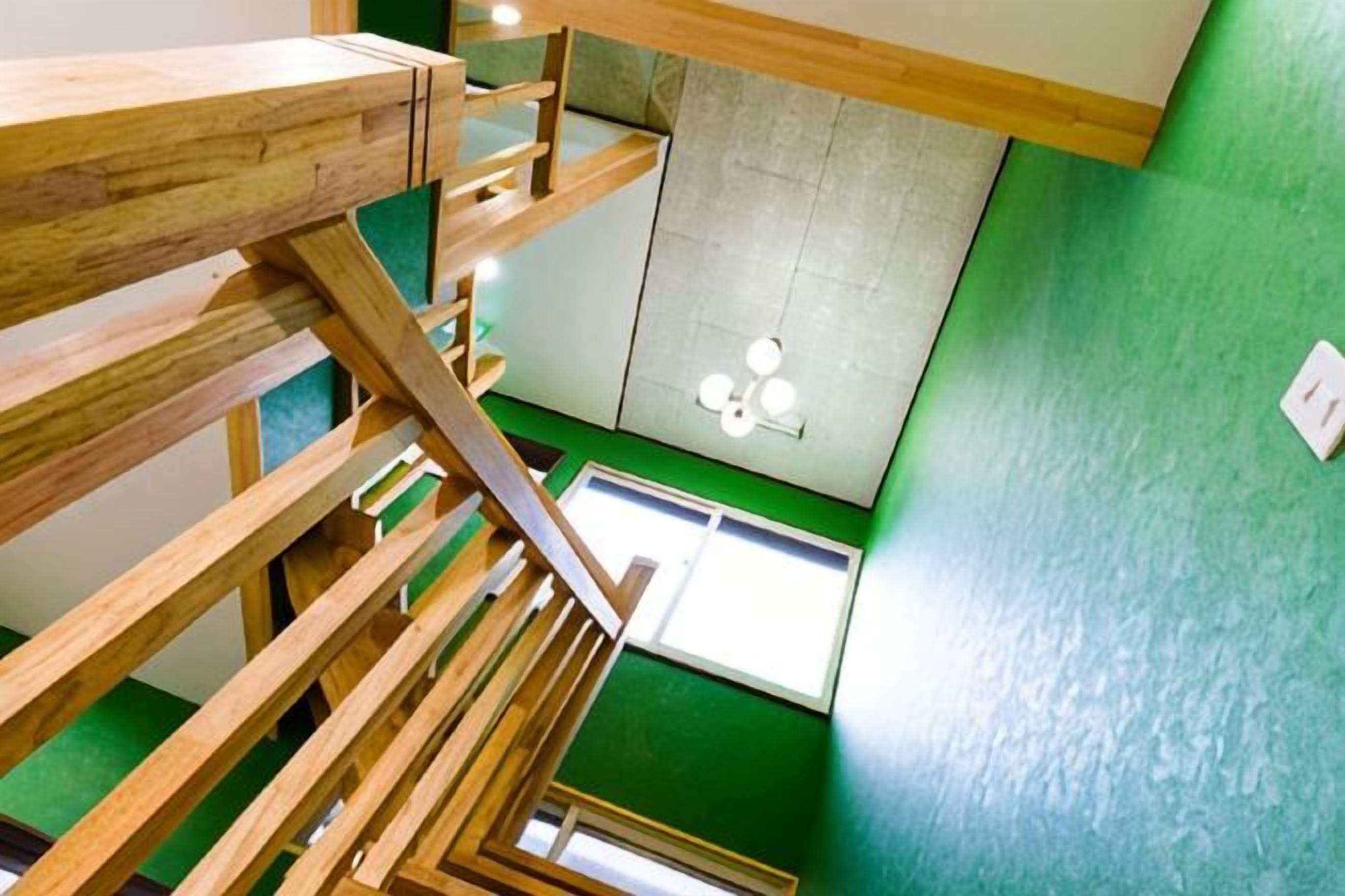 A multi-level wooden staircase with a view of a green wall and a ceiling light fixture.