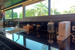 A modern kitchen with a large window, a glass sink, and a coffee machine.