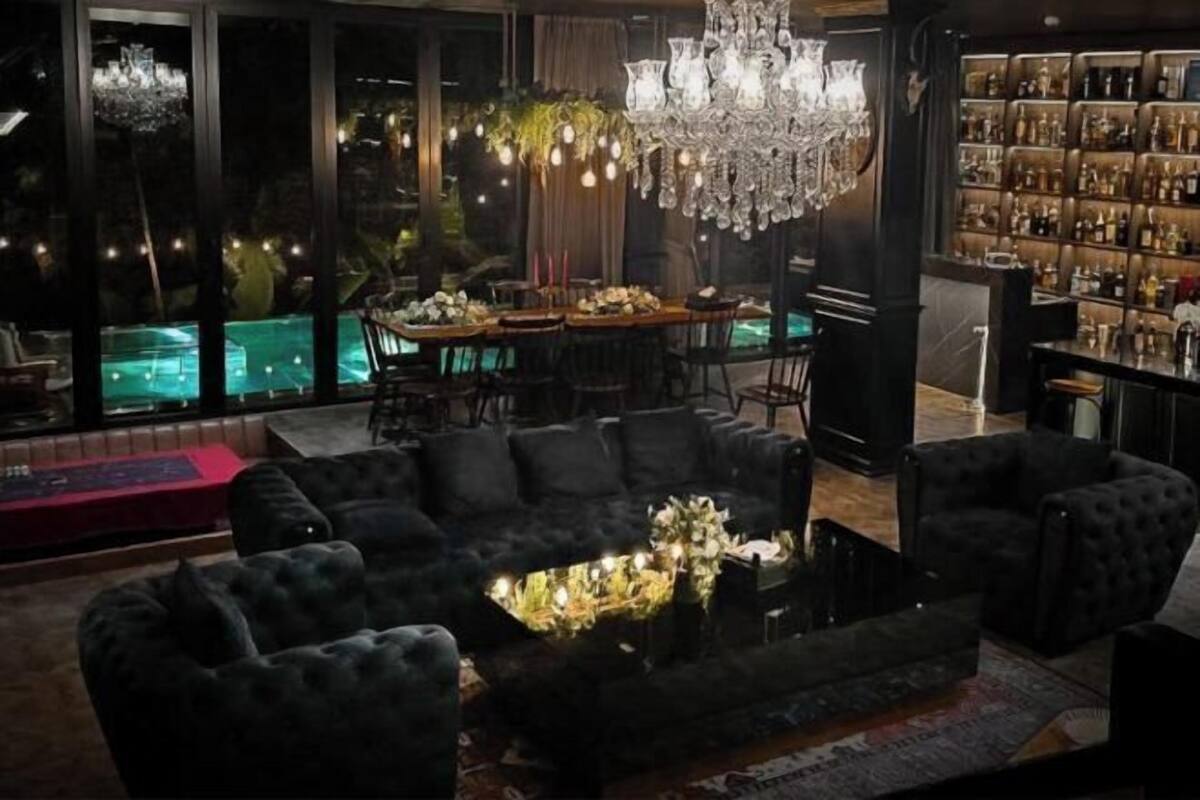 Un salon luxueux avec un grand canapé noir, un coin repas doté d’une table en bois et un bar avec des étagères remplies de bouteilles.