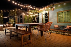 An outdoor patio with a wooden deck, wicker chairs, a dining table, and string lights. - The Black Kingdom (Bangkok)