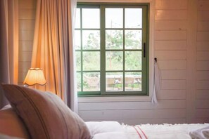 A bedroom with a bed, a window with curtains, and a lamp.