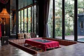 A room with a red table, a brown sofa, and large windows. - The Black Kingdom (Bangkok)