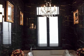 A luxurious bathroom with a large bathtub, a chandelier, and framed pictures on the walls. - The Black Kingdom (Bangkok)