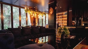 A cozy lounge area with a dark-colored sofa, a coffee table with a vase of flowers, and a bookshelf filled with books and decorative items. - The Black Kingdom (Bangkok)