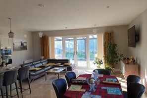 A modern living room with a sofa, dining table, chairs, and a kitchen area. - Aran Guesthouse - Kingsize Bed with Ensuite (Fingal)