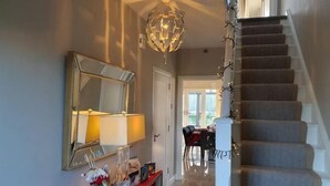 Een trap met een beklede binnenkant, een aan de muur bevestigde spiegel, een tafel met een lamp en een decoratief object op de consoletafel.