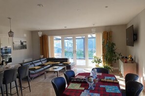 A modern living room with a sectional sofa, a dining table with chairs, and a kitchen area.