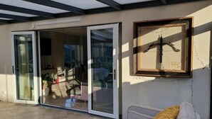 Een kamer met een schuifglasdeur naar een terras, een inlijsting foto aan de muur en een bank met kussens.