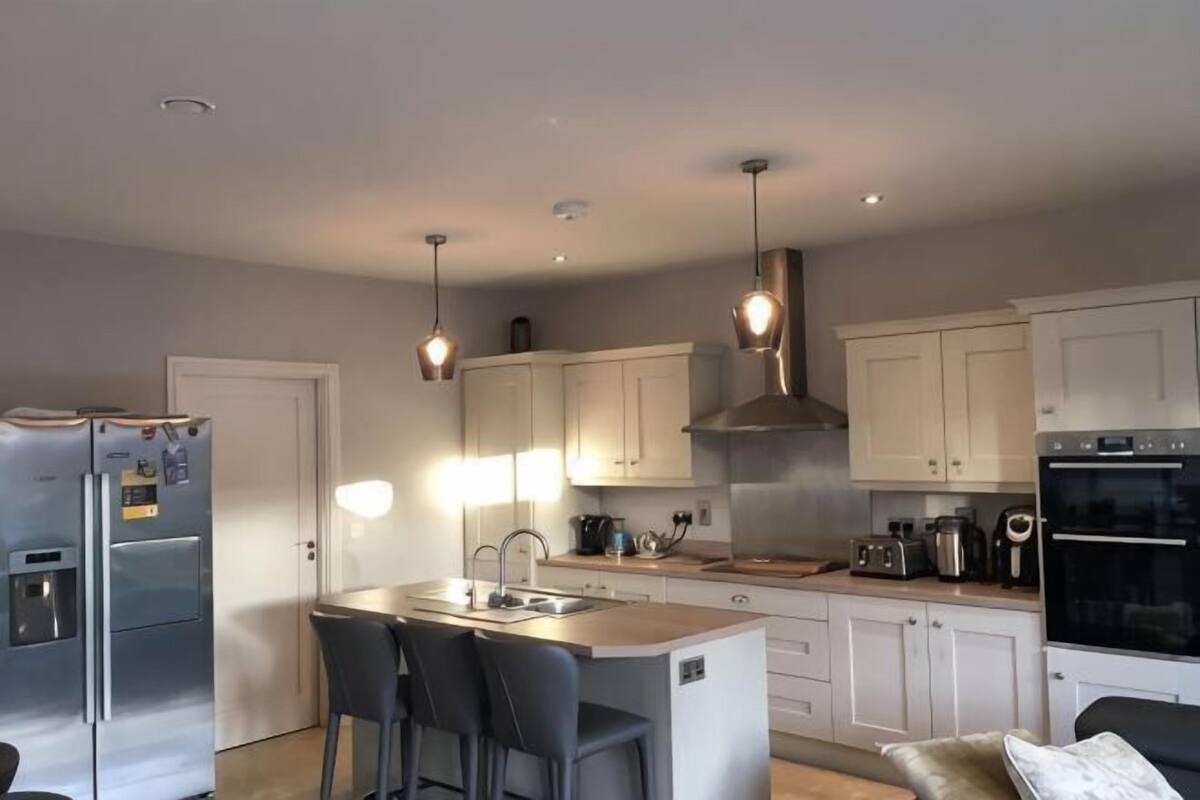 Une cuisine moderne dotée d’un îlot central, d’appareils électroménagers en acier inoxydable et de luminaires suspendus.