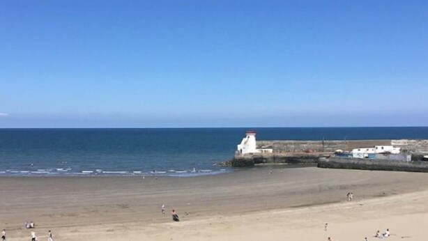 Een strand met een vuurtoren, zandstrand en rustige zee.