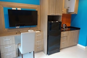 A modern kitchen with a flat-screen TV, a black refrigerator, and light wood cabinets. - 2 Bedroom Condo in Pattaya (Jomtien Area, Pratamnak Hill, New North European Trend 6 Hotel Condo) (Pattaya)