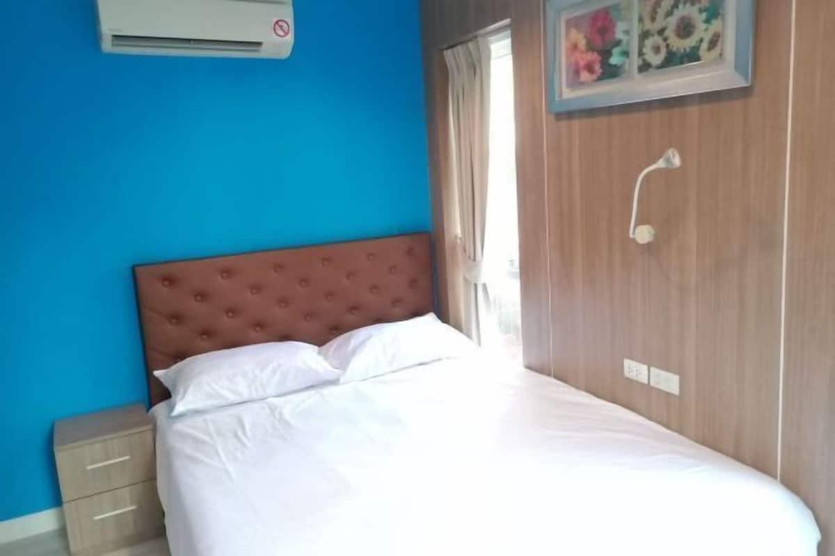 A bed with white linens, a wooden headboard, a nightstand, a wall-mounted air conditioner, and a window with curtains.
