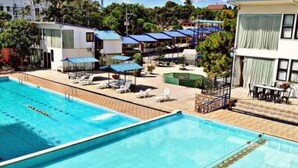 A swimming pool with lounge chairs and umbrellas, surrounded by buildings and greenery. - Brilliantsky Liesure Park and Hotel (Tagaytay)