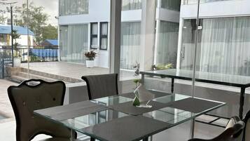 A modern outdoor dining area with a glass table and chairs, a view of a building, and a small plant on the table.