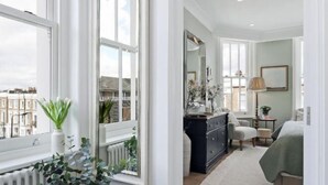 A spacious bedroom with a large window, a dresser, a chair, and a bed. - 317 Grand Maisonette (London)
