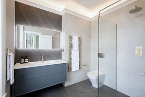 A modern bathroom with a glass-enclosed shower, a white sink, and a dark-toned vanity. - 317 Grand Maisonette (London)