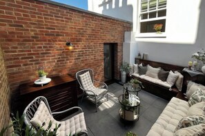 A patio with a brick wall, seating area with cushioned furniture, and a decorative table. - 317 Grand Maisonette (London)