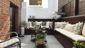 A cozy seating area with a cushioned sofa and a round table, surrounded by potted plants and a brick wall. - 317 Grand Maisonette (London)