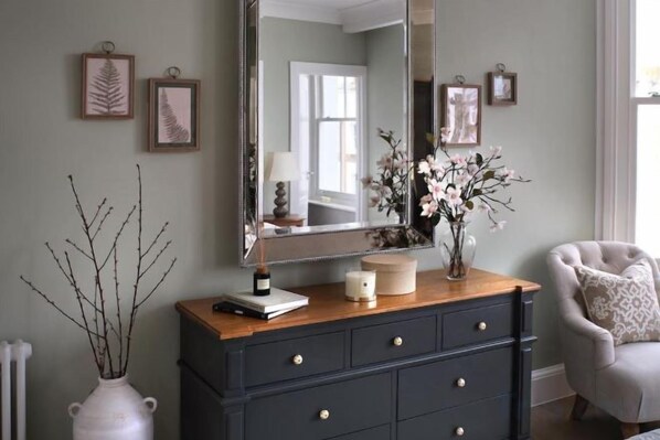 A dresser with a mirror, a vase with flowers, and a lamp. - 317 Grand Maisonette (London)