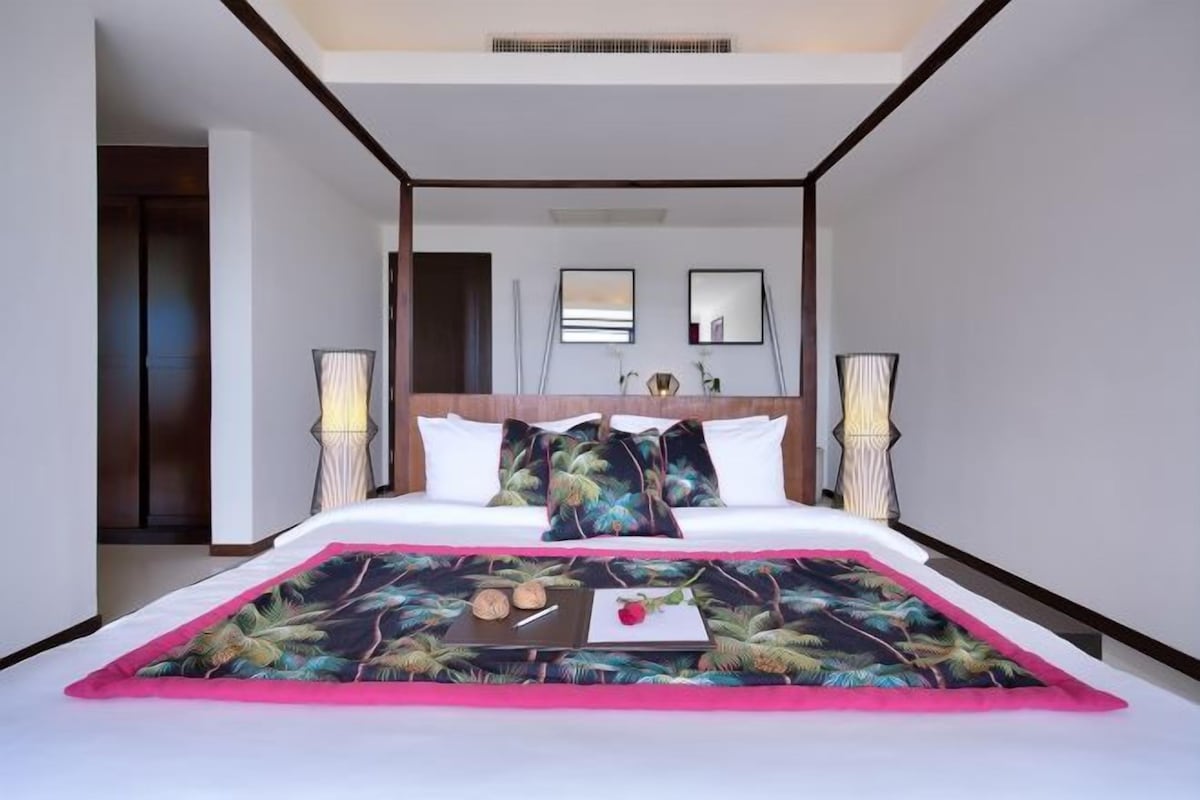 A modern hotel room with a large bed, two bedside lamps, and a view of the hallway.