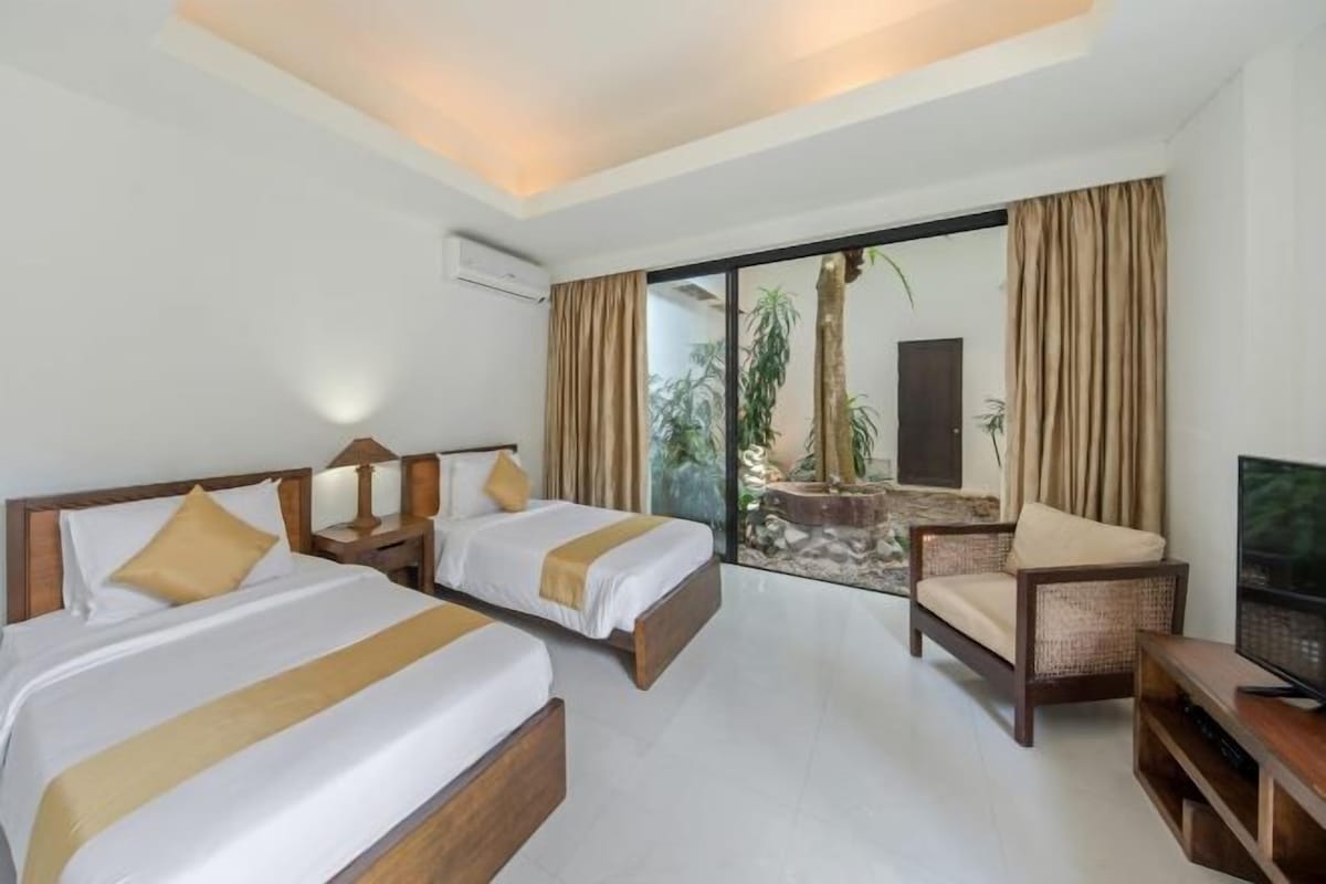 A hotel room with two beds, a TV, a chair, and a view of the outdoors.