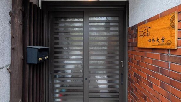 Dos puertas con listones horizontales, un letrero en la pared con caracteres chinos y un buzón pequeño y oscuro.