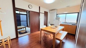 Una habitación con una mesa de comedor de madera, una pequeña cocina y una puerta corredera que da a otra habitación.