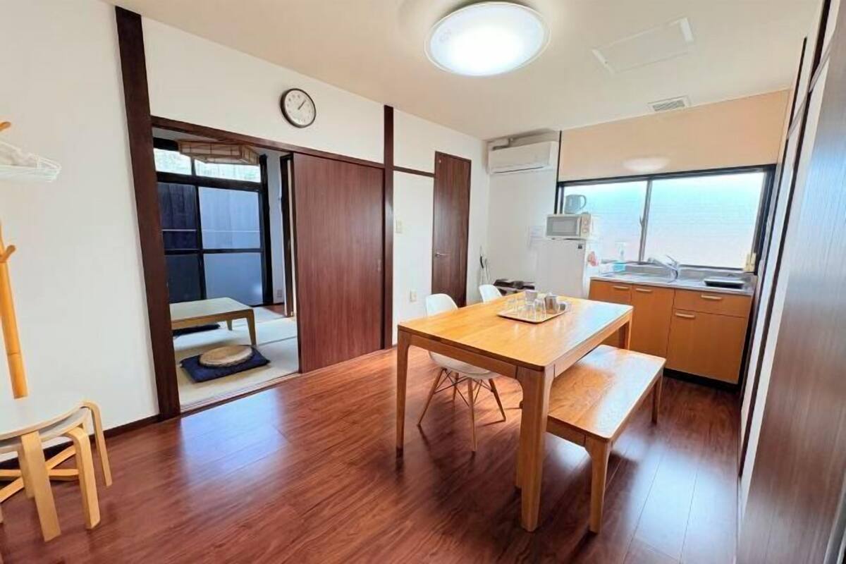 Habitació amb taula de menjador de fusta, una petita cuina i una porta corredissa que dona a una altra estança.