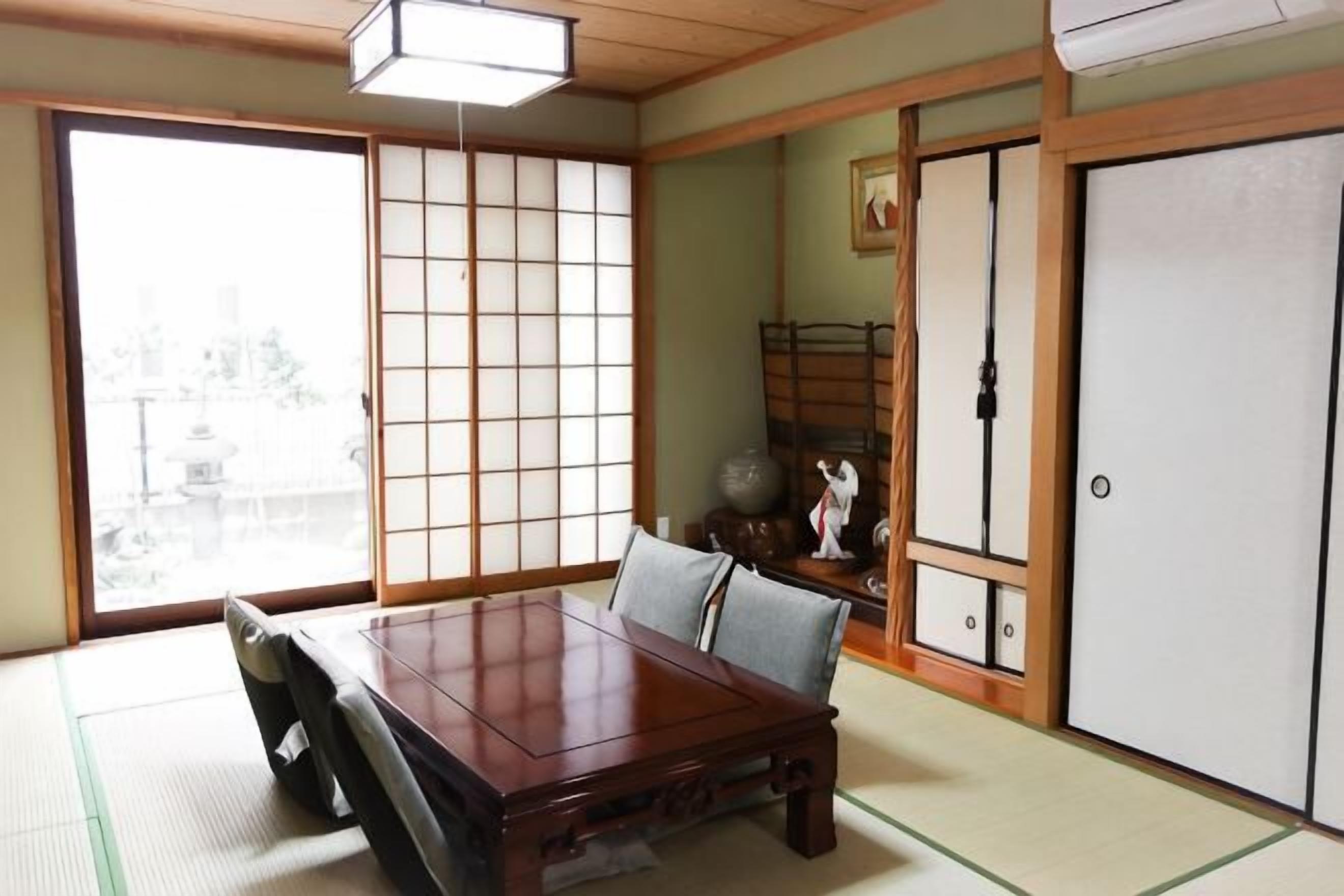 A traditional Japanese room with tatami flooring, a wooden table, sliding doors, and a view of the city.