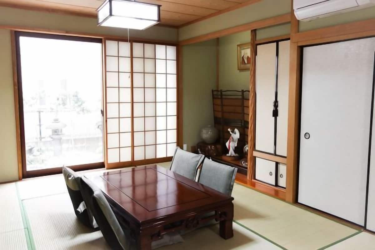 A traditional Japanese room with tatami flooring, a wooden table, sliding doors, and a view of the city.