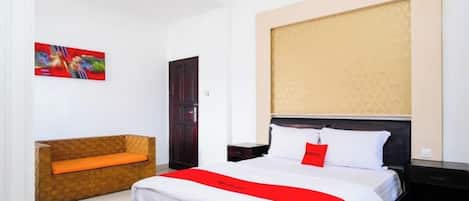 A hotel room with a large bed, a wooden bench, a painting on the wall, and a door.