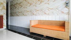 Een kamer met een wand in marmerlook, een rieten bank met oranje kussen, en een betegelde vloer.