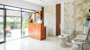 Een receptiegedeelte met een houten balie, witte rieten stoelen, een muur met marmerlook en een plafondventilator.