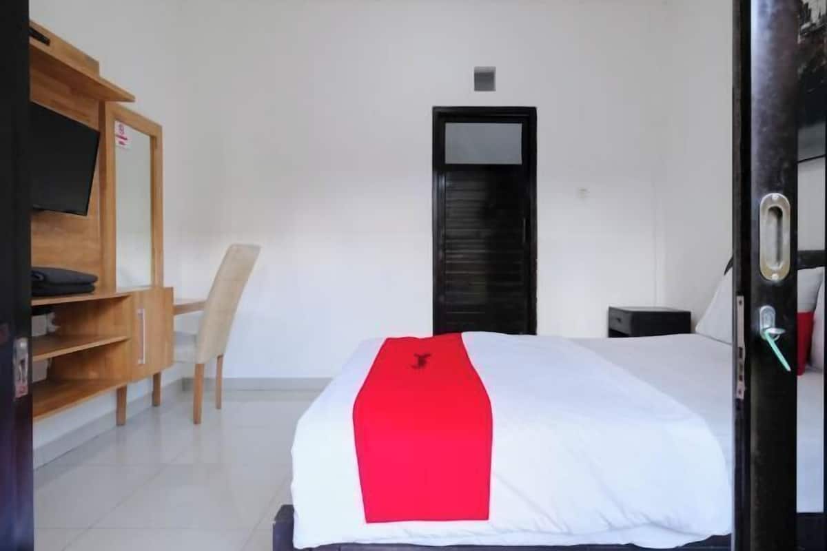 Une chambre d’hôtel avec un lit, un bureau en bois, une chaise, une télévision et une porte.