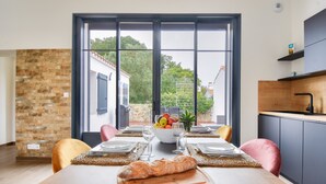 A dining area with a wooden table set for two, a bowl of fruit, and a baguette on a cutting board. - Beach 400 m away - House for 4 with terrace (La Guérinière)