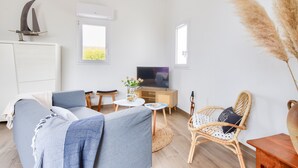 A living room with a sofa, a television, a wicker chair, and a small table with a vase of flowers. - Beach 400 m away - House for 4 with terrace (La Guérinière)