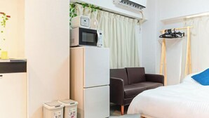 A compact hotel room with a bed, a sofa, a microwave, a small fridge, and a trash bin. - Motomachi Hisui Building (Yokohama)