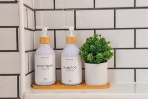 Two bottles of body wash and shampoo on a shelf with a small potted plant. - The value of time pool villa Khaoyai (Pak Chong)