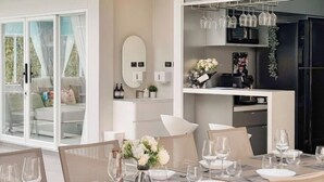 A modern dining area with a table set for four, a kitchen area with wine glasses on a shelf, and a sliding glass door leading to a balcony. - The value of time pool villa Khaoyai (Pak Chong)