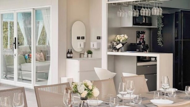 Ein moderner Essbereich mit einem Tisch für vier Personen, ein Küchenbereich mit Weingläsern in einem Regal und eine Glastür zum Balkon.