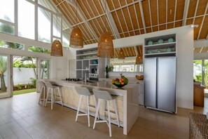 Une cuisine moderne avec un coin bar, des tabourets de bar blancs, un grand réfrigérateur et des luminaires suspendus.